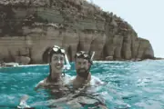 Two snorkeling guests at the surface below coastal cliffs