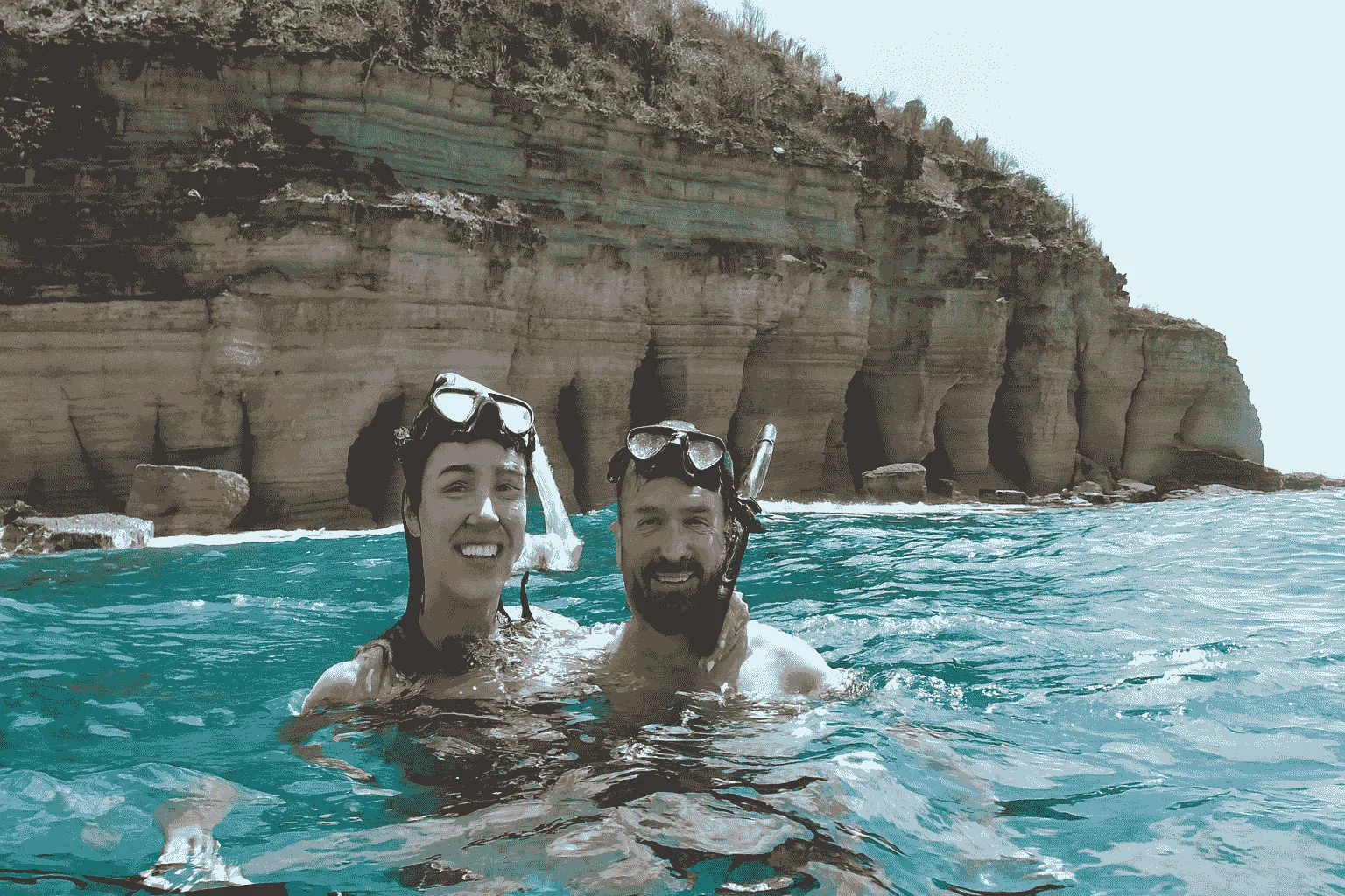 Two snorkeling guests at the surface below coastal cliffs