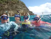 Four guests snorkeling together beside coastal rock formations