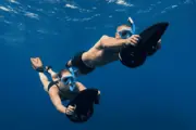 Two snorkelers holding powered sea scooters in blue water