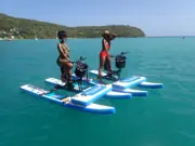 Two guests riding Sea Cycle water bikes beside the green coastline