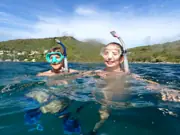 Two snorkelers at the surface with the Antigua coastline behind them